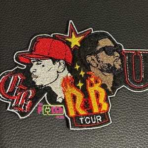 May include: An embroidered patch featuring two figures, one wearing a red cap, with the text "OG" in red, "R&B" in yellow and orange flames, "T'OUR" in white, and a large "U" in red and black, accented by a yellow star and small yellow stars.