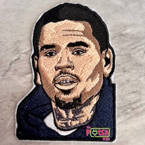 May include: Embroidered patch featuring a portrait of a man with a dark complexion, short black hair, and a goatee. He is wearing a dark blue hoodie. The patch has a white border and a small logo in the bottom right corner that reads "TM PLUG PATCH".
