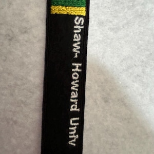 May include: Black embroidered patch with a white "M" and yellow and green stripes. The text "Shawnt Howard Univ" is embroidered in white on the patch.