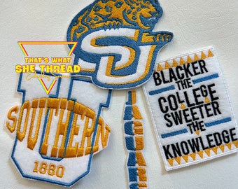 Può includere: Tre toppe ricamate con sfondo bianco e cuciture blu e dorate. La prima toppa presenta un giaguaro con le lettere "SU" sullo sfondo. La seconda toppa presenta la parola "SOUTHERN" con l'anno "1880" sotto. La terza toppa presenta il testo "Blacker the College Sweeter the Knowledge".