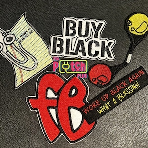 May include: A collection of embroidered patches including a paperclip character on lined paper, a white and black BUY BLACK patch, a yellow and red tennis racket, a red FB logo, and a black rectangular patch with the text WOKE UP BLACK AGAIN WHAT A BLESSING.