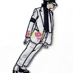May include: Embroidered patch featuring a stylized depiction of a performer in a white suit, black tie, and fedora. The patch includes the text "Tha Patch Plug" in a colorful design. The figure is in a dynamic pose, suggesting movement.