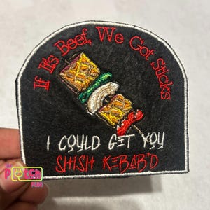 May include: Black embroidered patch with the text "If It's Beef, We Got Sticks" and "I Could Get You Shish Kebab'd". The patch features a colorful embroidered image of a shish kebab. The patch is a fun, food-themed accessory.