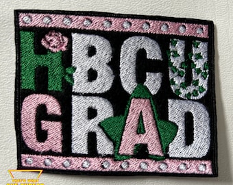 Può includere: Una toppa ricamata da stirare con le parole "HBCU GRAD" in lettere rosa, verdi e bianche su uno sfondo nero. La toppa ha un bordo rosa con punti bianchi.