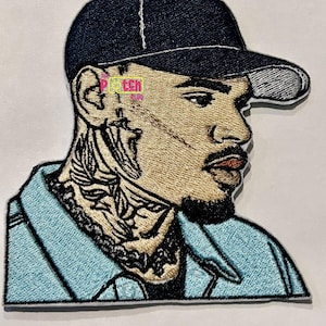 May include: An embroidered patch featuring a portrait of a man wearing a blue baseball cap and a light blue shirt. The man has a beard and tattoos on his neck.