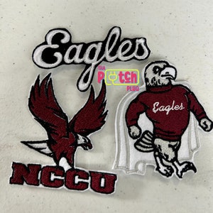 May include: Three embroidered patches featuring the word "Eagles" in white script on a black background, a maroon eagle with outstretched wings, and a maroon eagle mascot wearing a sweater with "Eagles" on it. The patches are on a light gray surface.