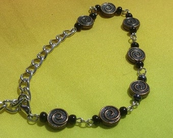 Könnte beinhalten: Ein silbernes Kettenarmband mit schwarzen Perlen und silbernen Wirbel-Anhängern.