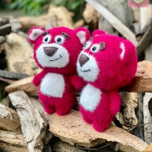 May include: Two handmade, plush pink teddy bears with white bellies and brown noses and eyebrows. The bears are standing on a bed of wood. The bears have black eyes and are smiling. The bears are a handmade craft.
