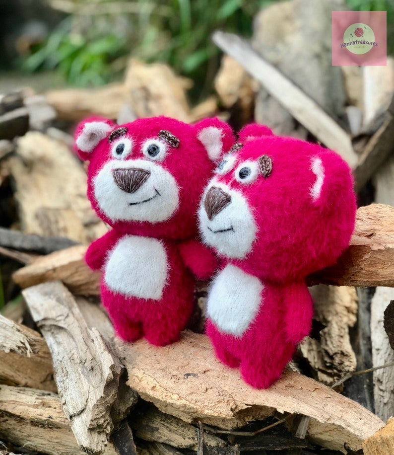 Puede incluir: Dos osos de peluche rosas hechos a mano, con vientres blancos y narices y cejas marrones. Los osos est&aacute;n sobre una cama de madera. Los osos tienen ojos negros y est&aacute;n sonriendo. Los osos son una artesan&iacute;a hecha a mano.