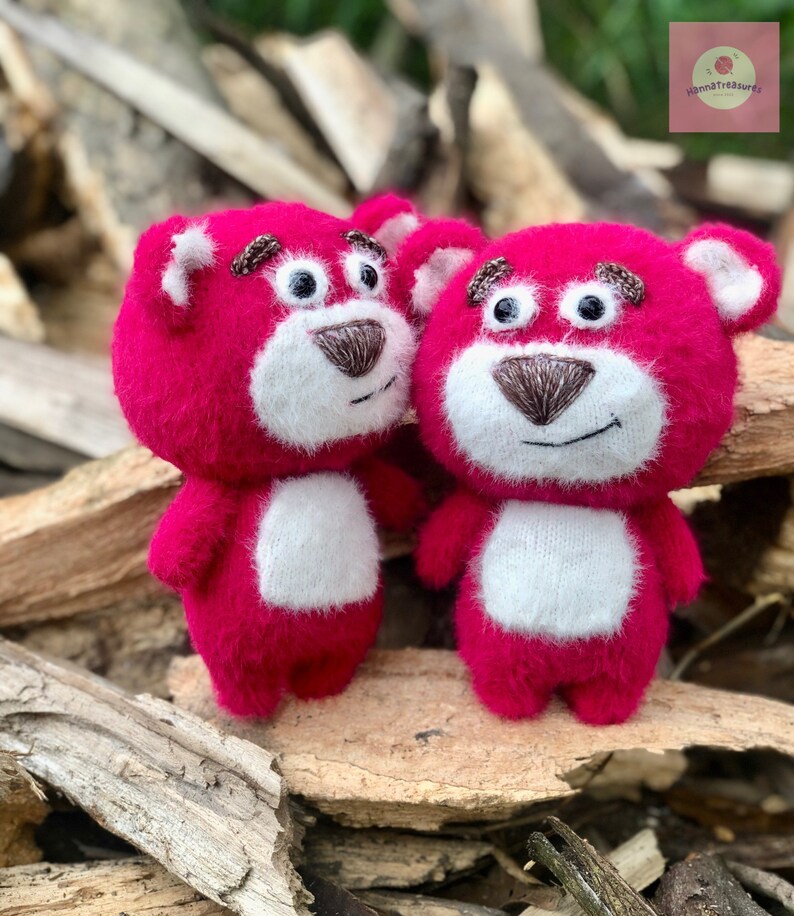 Puede incluir: Dos osos de peluche rosas con vientres y caras blancas. Los osos tienen narices y cejas marrones bordadas y ojos negros. Los osos est&aacute;n de pie sobre un trozo de madera.