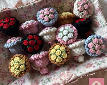 Op de afbeelding: Een verzameling gehaakte bloemboeketten in verschillende kleuren, waaronder rood, roze, wit en geel. De boeketten zijn gerangschikt in een bloempatroonmand. De afbeelding bevat een roze vierkant met de tekst "HannaTreasures".