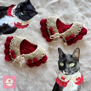 May include: Crocheted cat collars in red and cream with cherry accents. The collars are displayed on a white fluffy surface, with two black cats wearing the collars. The collars have a scalloped edge and a tie closure.