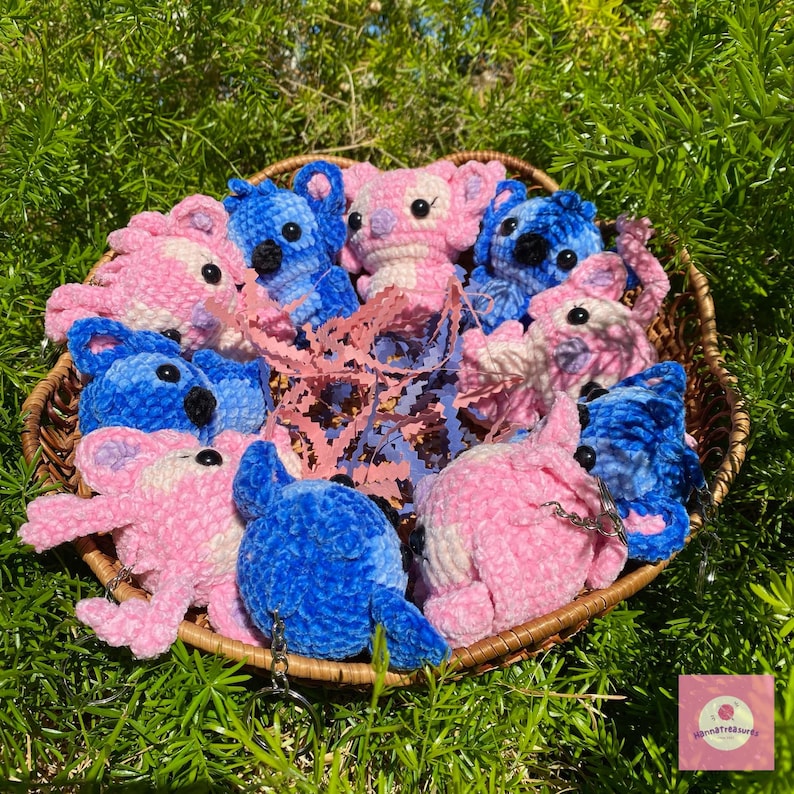 Puede incluir: Una cesta de mimbre llena de koalas y criaturas alien&iacute;genas de peluche hechos a mano en tonos rosa y azul. Los peluches tienen ojos negros y est&aacute;n colocados sobre papel rosa. La cesta est&aacute; sobre hierba verde.