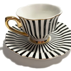 May include: A black and white striped teacup and saucer set with gold trim. The cup and saucer have a vertical stripe pattern.