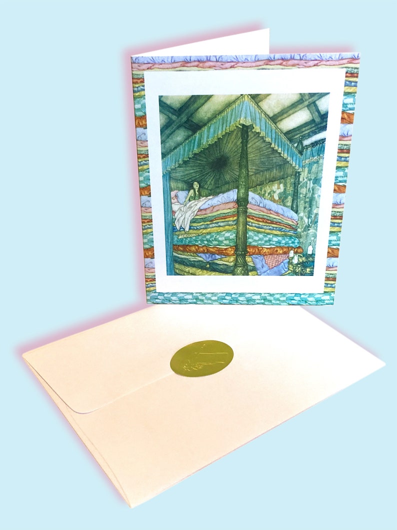 May include: A fairytale-themed greeting card showing a princess in a bed of many mattresses. The card has a decorative border and is accompanied by a cream envelope with a gold seal. The illustration depicts a canopy bed in a room.