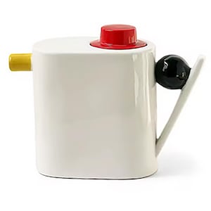 May include: A white ceramic teapot with a rounded rectangular body, featuring a small yellow spout on the left side, a bright red circular lid on top, and a black spherical accent attached to a white angled handle on the right side.