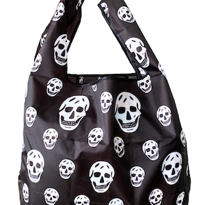 May include: Black tote bag with white skull pattern. The reusable shopping bag has two black handles and is made of a lightweight material. The bag is designed with a repeating pattern of white skulls on a black background.
