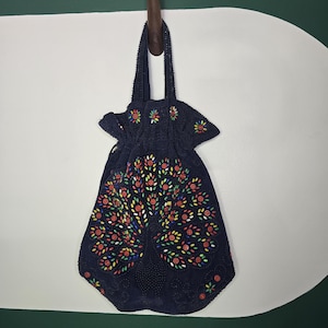 Puede incluir: Un bolso de mano azul oscuro con cuentas y un diseño de árbol floral. El árbol está adornado con cuentas de colores rojo, amarillo y verde. El bolso tiene un cierre de cordón y un asa de cuentas.