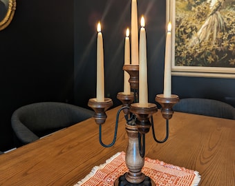 Puede incluir: Un candelero de madera con seis brazos para velas y una base de metal negro. El candelero está decorado con un patrón floral y tiene seis velas encendidas.