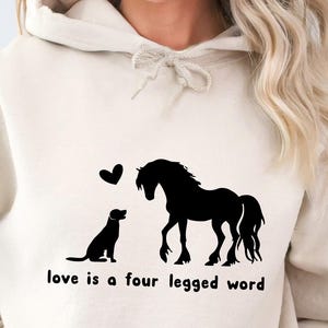 May include: A cream-coloured hoodie with a black silhouette of a horse and dog with hearts above them. The text "love is a four legged word" is printed below the image.