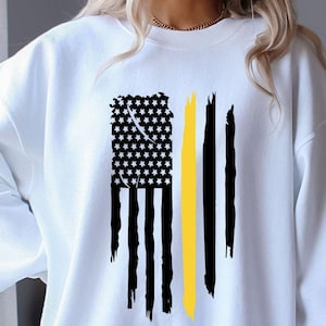 May include: White sweatshirt featuring a distressed American flag design with a yellow stripe. The flag has a black and white star field and black stripes. The sweatshirt is a casual, comfortable style.