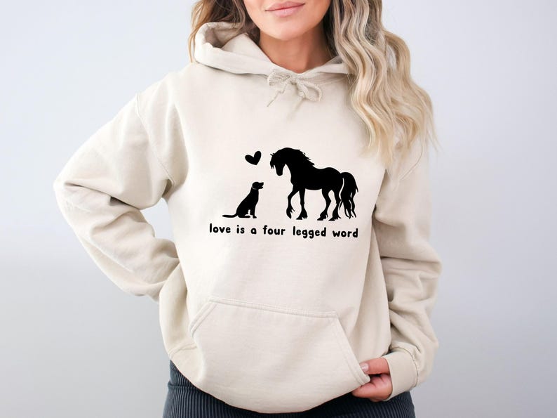 May include: A cream-coloured hoodie with a black silhouette of a horse and dog with hearts above them. The text "love is a four legged word" is printed below the image.