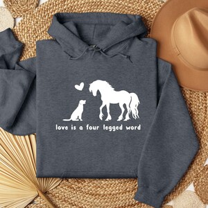 May include: A dark grey hoodie with a white graphic of a horse and dog with a heart above them. The text "love is a four legged word" is below the graphic.