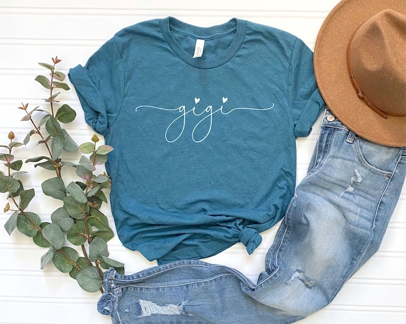 May include: Teal blue t-shirt with a white cursive font that says "gigi" with two small white hearts above the word.