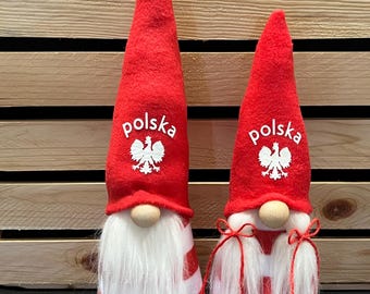 Może przedstawiać: Dwa czerwono-białe pasiastych krasnoludków z białymi brodami i czerwonymi czapkami. Czapki mają polską flagę i napis "polska" na nich.