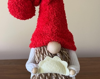 May include: A red and white gnome with a long brown beard holding a yellow felt crescent-shaped object.