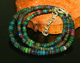 May include: A multi-strand necklace made of small, round, iridescent opal beads in shades of green, blue, and black. The necklace is strung on a silver chain with a lobster clasp.