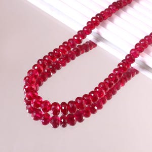 May include: A strand of faceted, deep red gemstone beads arranged in a double loop. Each individual bead features a circular shape with multiple cut facets that reflect light, creating a consistent, vibrant crimson appearance throughout the strand.