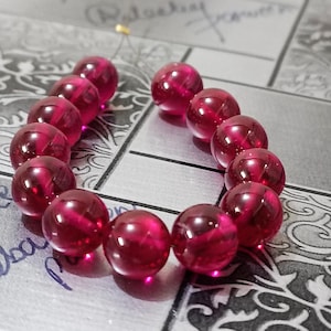 Puede incluir: Un brazalete hecho de cuentas de piedras preciosas de color rojo intenso. Las cuentas son redondas y tienen un acabado brillante.