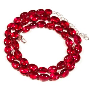 May include: A red gemstone necklace with oval-shaped beads. The necklace is made of a silver chain with a clasp.