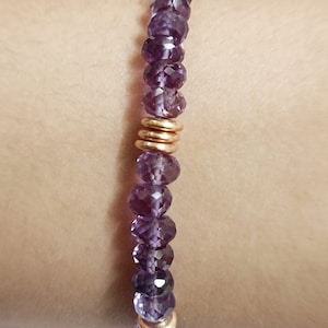 May include: A purple gemstone bracelet with gold accents. The bracelet is made of small, faceted beads and is strung on a stretchy cord.