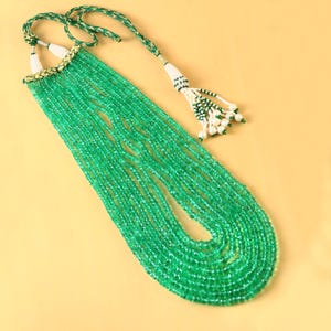Peut inclure: Un long collier multi-rangs composé de perles de pierres précieuses vertes. Le collier a un pompon avec des perles blanches et vertes à l'extrémité.