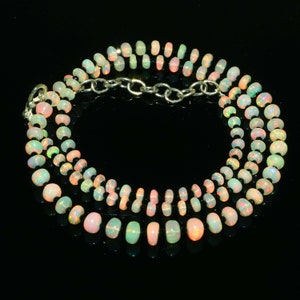 May include: A necklace composed of multiple strands of opal beads in various sizes. The beads display a range of colors, including white, pink, and hints of green and orange. The necklace is connected by a silver chain clasp.