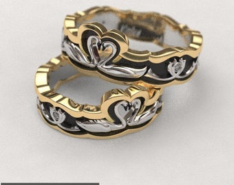 May include: Two gold rings with a black enamel band and a white swan design. The swans are facing each other and have a heart shape in the middle. The rings are stacked on top of each other.