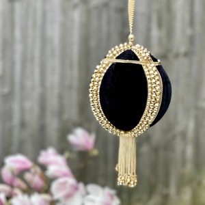 May include: A black velvet clutch bag with a gold chain strap and tassel. The bag is decorated with gold beads.