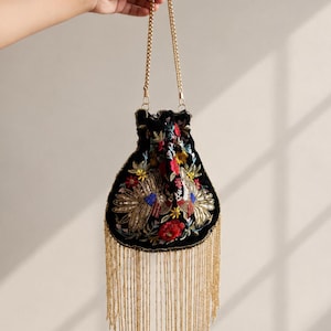 May include: Black velvet handbag with gold beaded fringe and a gold chain strap. The bag is adorned with colorful floral embroidery and the word "MAGNOLIA" is printed at the bottom.