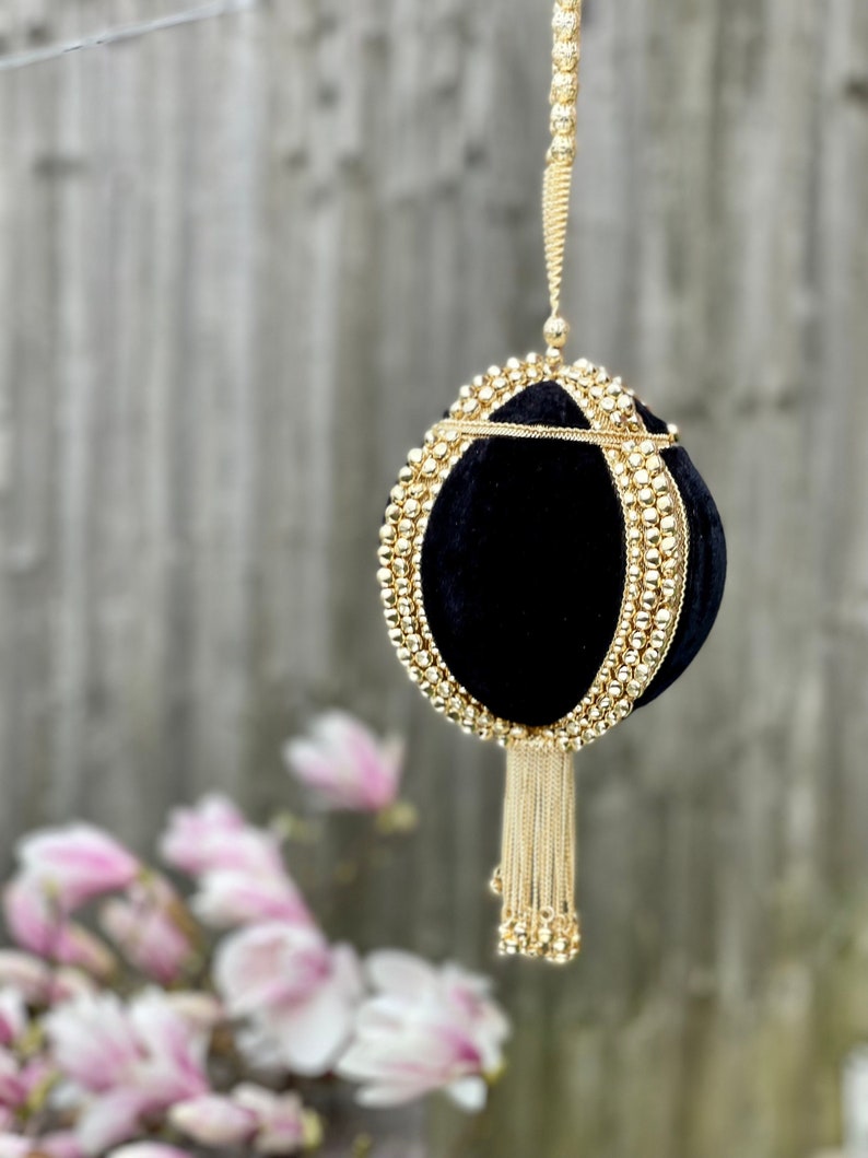 May include: A black velvet clutch bag with a gold chain strap and tassel. The bag is decorated with gold beads.