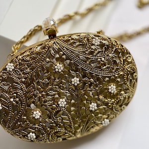 May include: A gold metal clutch bag with an intricate floral design and white pearl accents. The bag has a chain strap.
