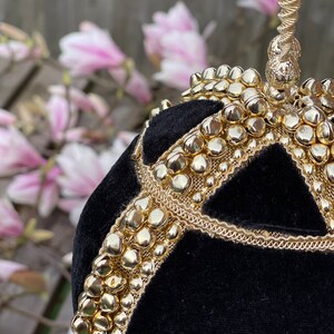 May include: A black velvet evening bag with a gold chain handle and gold embellishments. The bag is round and has a geometric design.