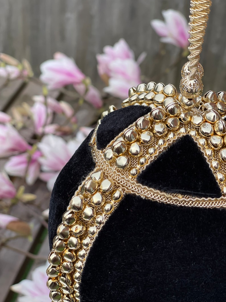 May include: A black velvet evening bag with a gold chain handle and gold embellishments. The bag is round and has a geometric design.