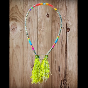 Puede incluir: Un collar único con un diseño colorido de cuentas. El collar presenta una sección superior de colores del arcoíris y un estampado de leopardo. La parte inferior tiene borlas amarillas brillantes y un cierre de metal plateado. El collar se muestra sobre un fondo de madera.