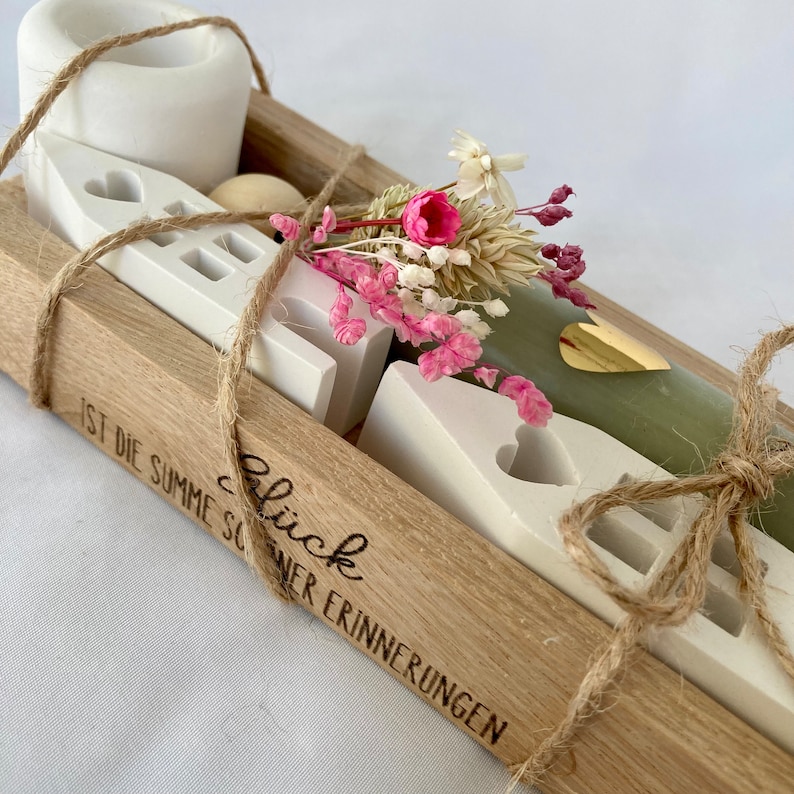 Peut inclure: Une bo&icirc;te en bois contenant une bougie vert clair, des maisons en c&eacute;ramique blanche et des fleurs s&eacute;ch&eacute;es. La bo&icirc;te est attach&eacute;e avec de la ficelle et porte la mention "Gl&uuml;ck ist die Summe sch&ouml;ner Erinnerungen" grav&eacute;e sur le c&ocirc;t&eacute;.