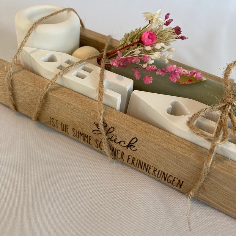 Peut inclure: Une bo&icirc;te en bois &agrave; la finition naturelle, attach&eacute;e avec de la ficelle, contient des maisons en c&eacute;ramique blanche, une petite boule en bois et des fleurs s&eacute;ch&eacute;es. La bo&icirc;te est grav&eacute;e du texte "Gl&uuml;ck ist die Summe sch&ouml;ner Erinnerungen".
