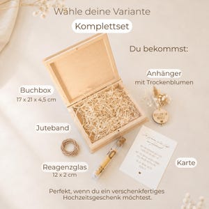 May include: A gift set containing a light-colored wooden book box measuring 17 x 21 x 4.5 cm filled with straw, a coil of jute twine, a 12 x 2 cm glass test tube with a cork stopper, a dried flower tag, and a white card with printed German text.