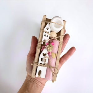 Peut inclure: Une petite bo&icirc;te en bois remplie d'une bougie rose, une maison en c&eacute;ramique blanche, des fleurs s&eacute;ch&eacute;es et un charme en forme de c&oelig;ur dor&eacute;. La bo&icirc;te est attach&eacute;e avec de la ficelle.