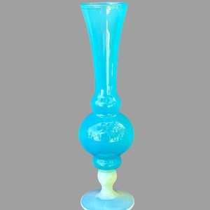 May include: A tall, blue glass vase with a white base. The vase has a bulbous middle section and a narrow neck.